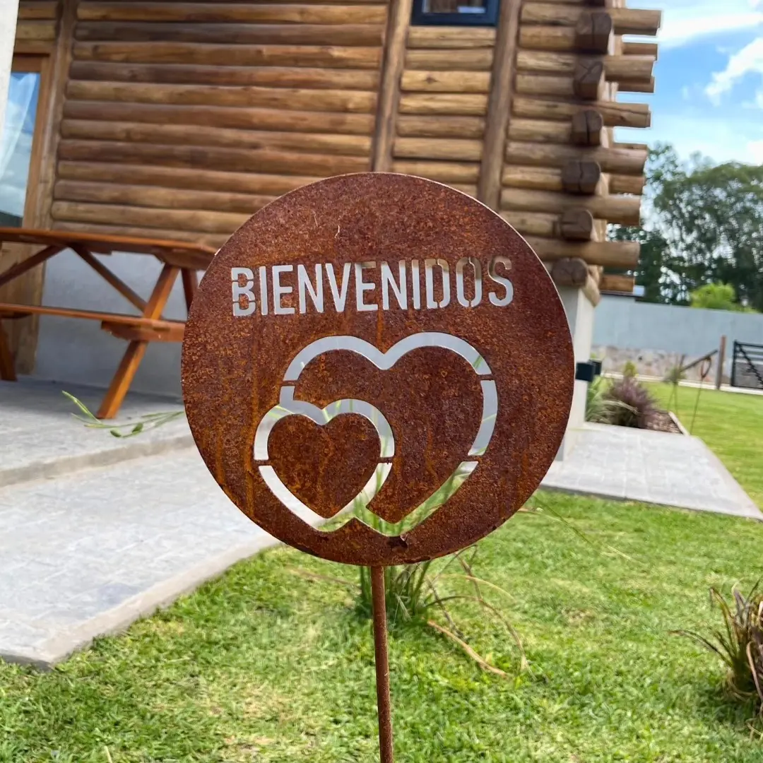 El cartel de chapa con la palabra Bienvenidos y dos corazones, en el parque frente a la galería.